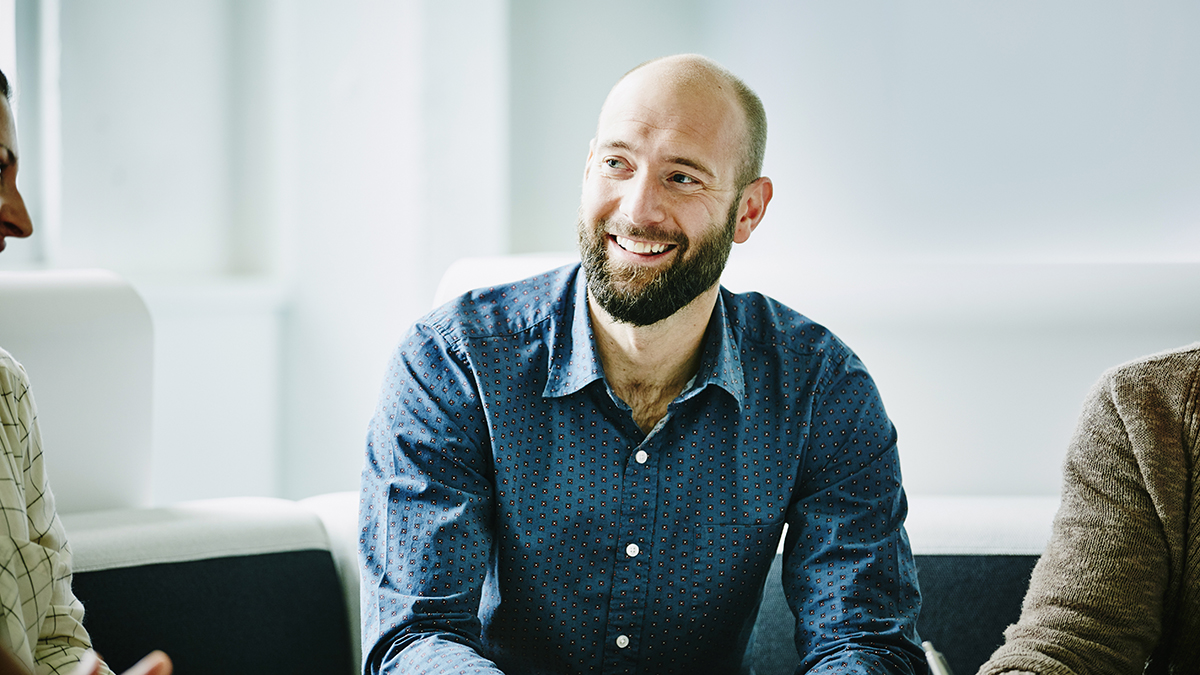 Man in his 30s smiling at work, sitting at desk