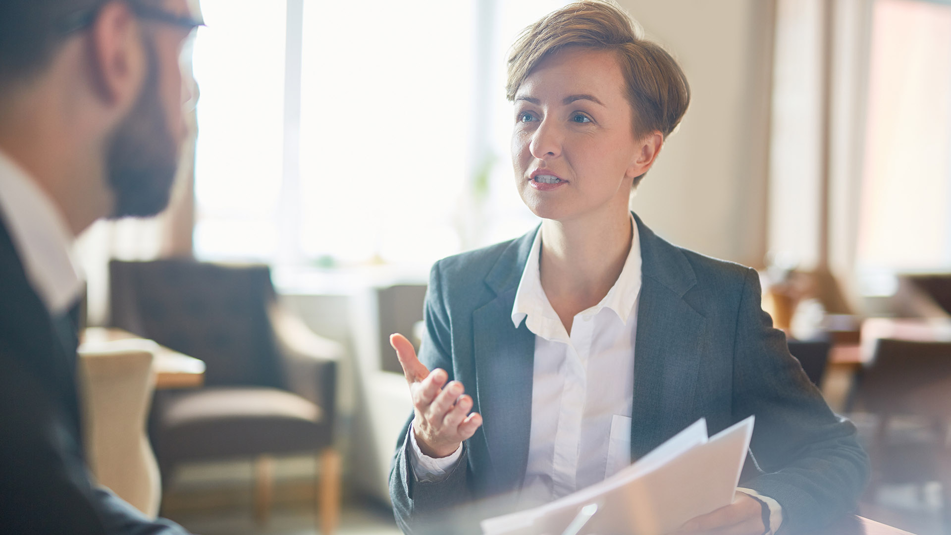Woman with short hair in a suit providing advice to a man across the table