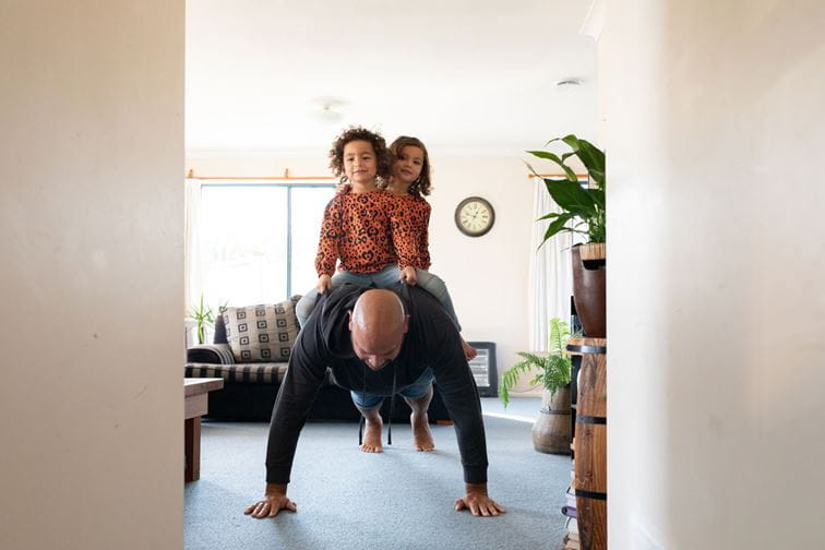Dad doing push-ups with twin daughters on his back