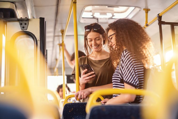 Two young women on public transport looking at a mobile together smiling