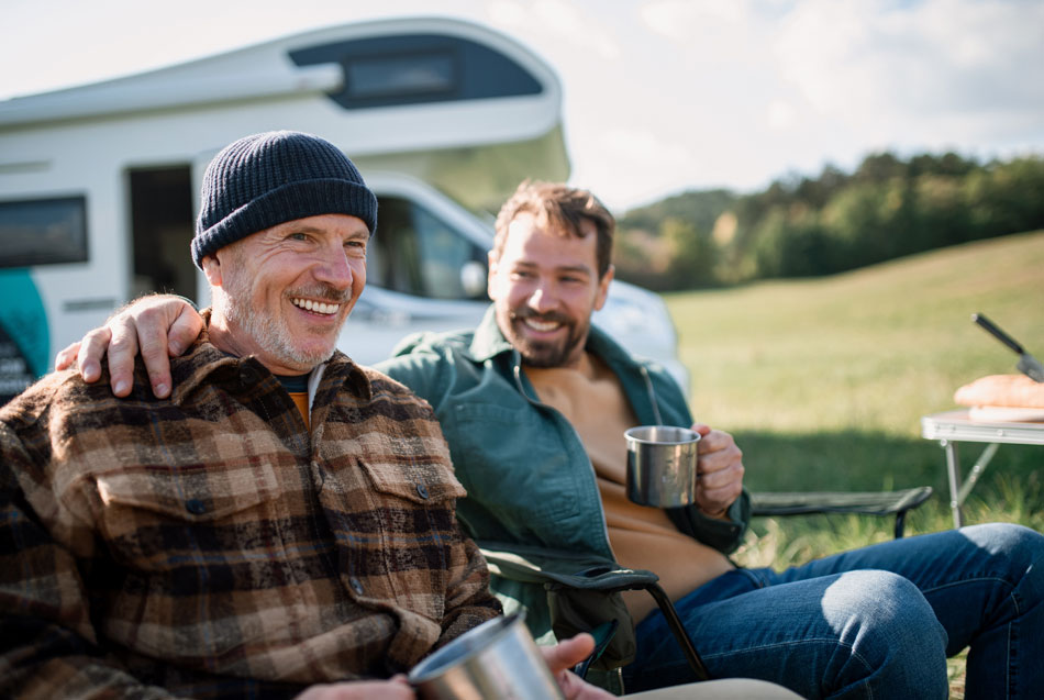 Two men sitting in front of a campervan enjoying a drink