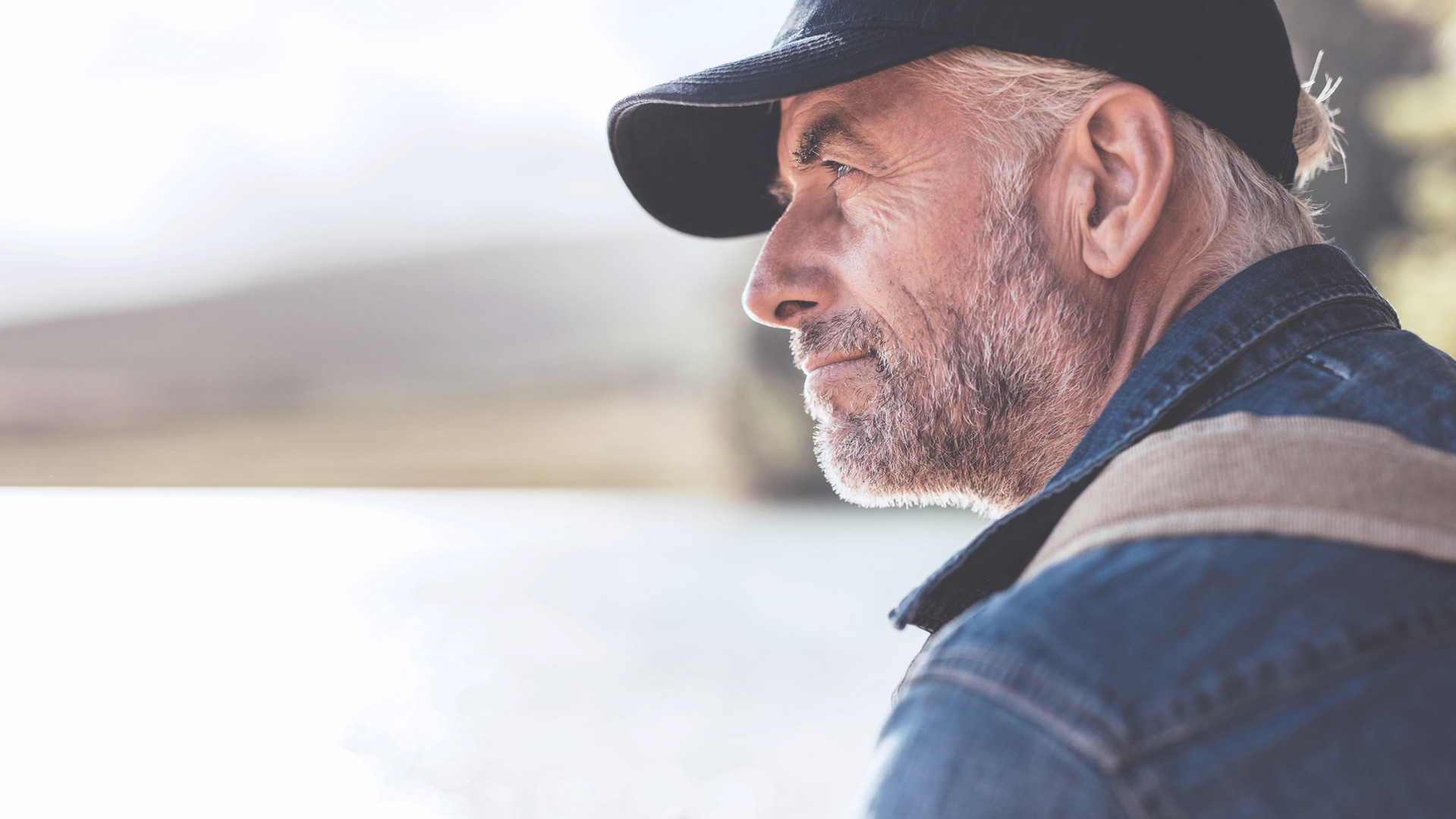 a man wearing a black hat and a denim jacket looking at the distance
