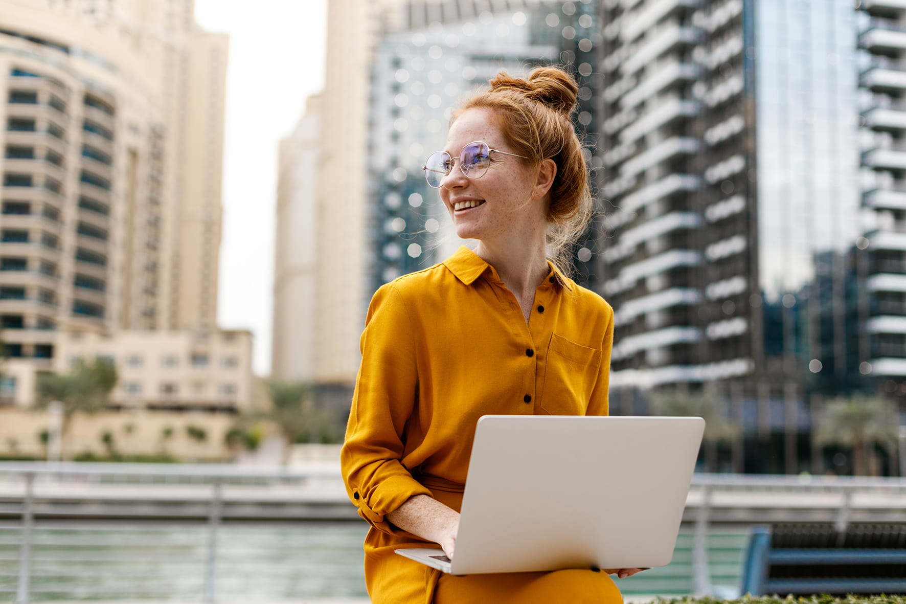 Woman with computer sitting in front of a river in the city