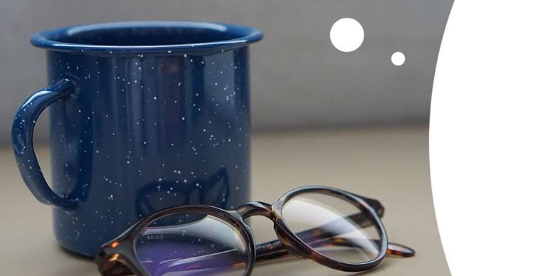 A blue cup stands next to pair of glasses on a desk